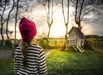 Girl with red hat and blue and white strip shirt looking at treehouse